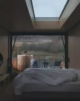 Photo de l'intérieur d'un lodge donnant sur la terrasse, la lumière est douce, on y aperçoit une femme profitant du bain nordique.